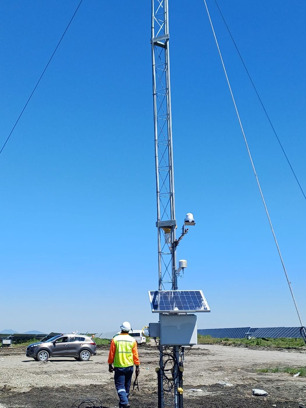 Technician at a guyed meteorological and communications mast with sensors, camera and solar-powered cabinet at a solar plant