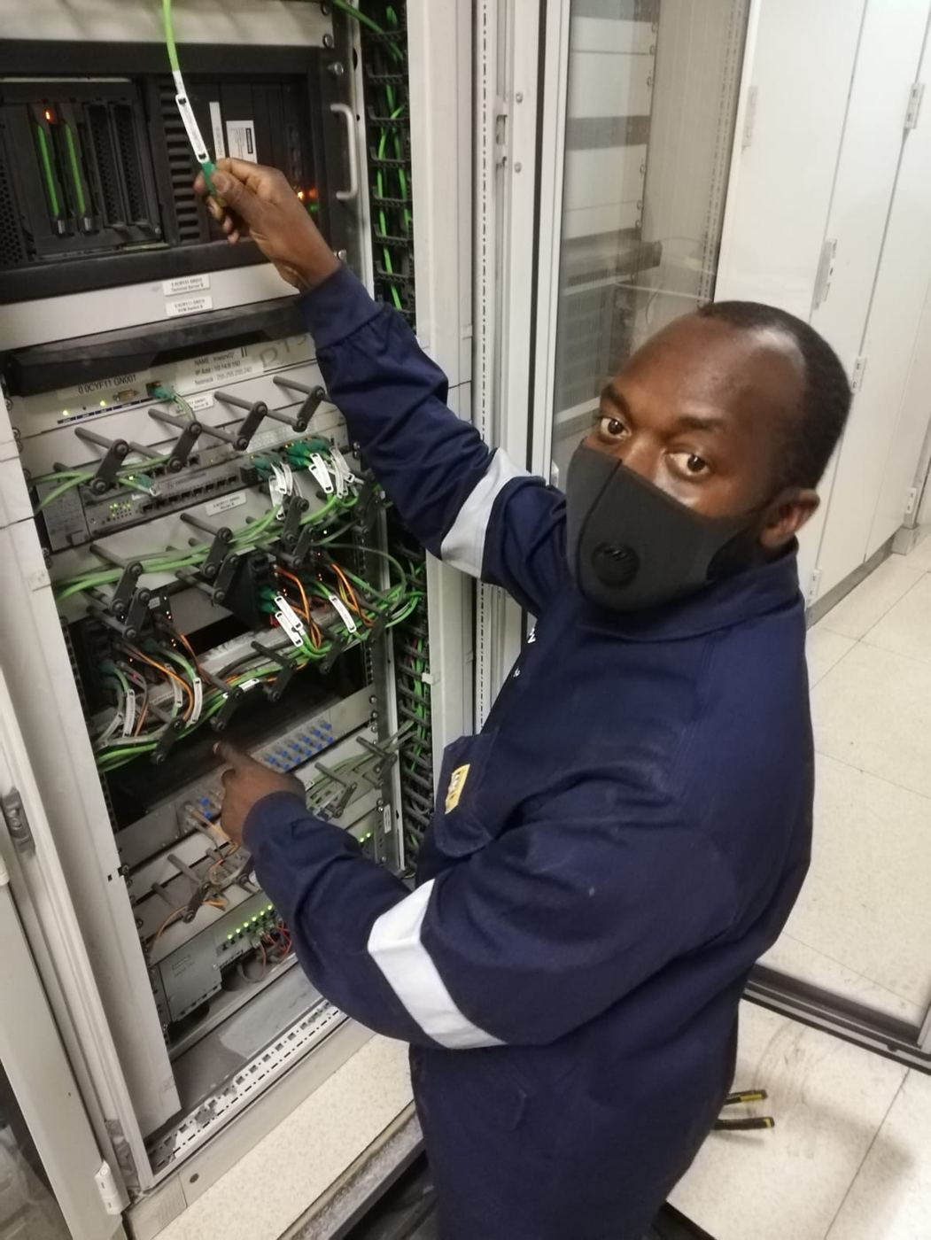 Gigatron technician in overalls patching a labelled industrial network cabinet