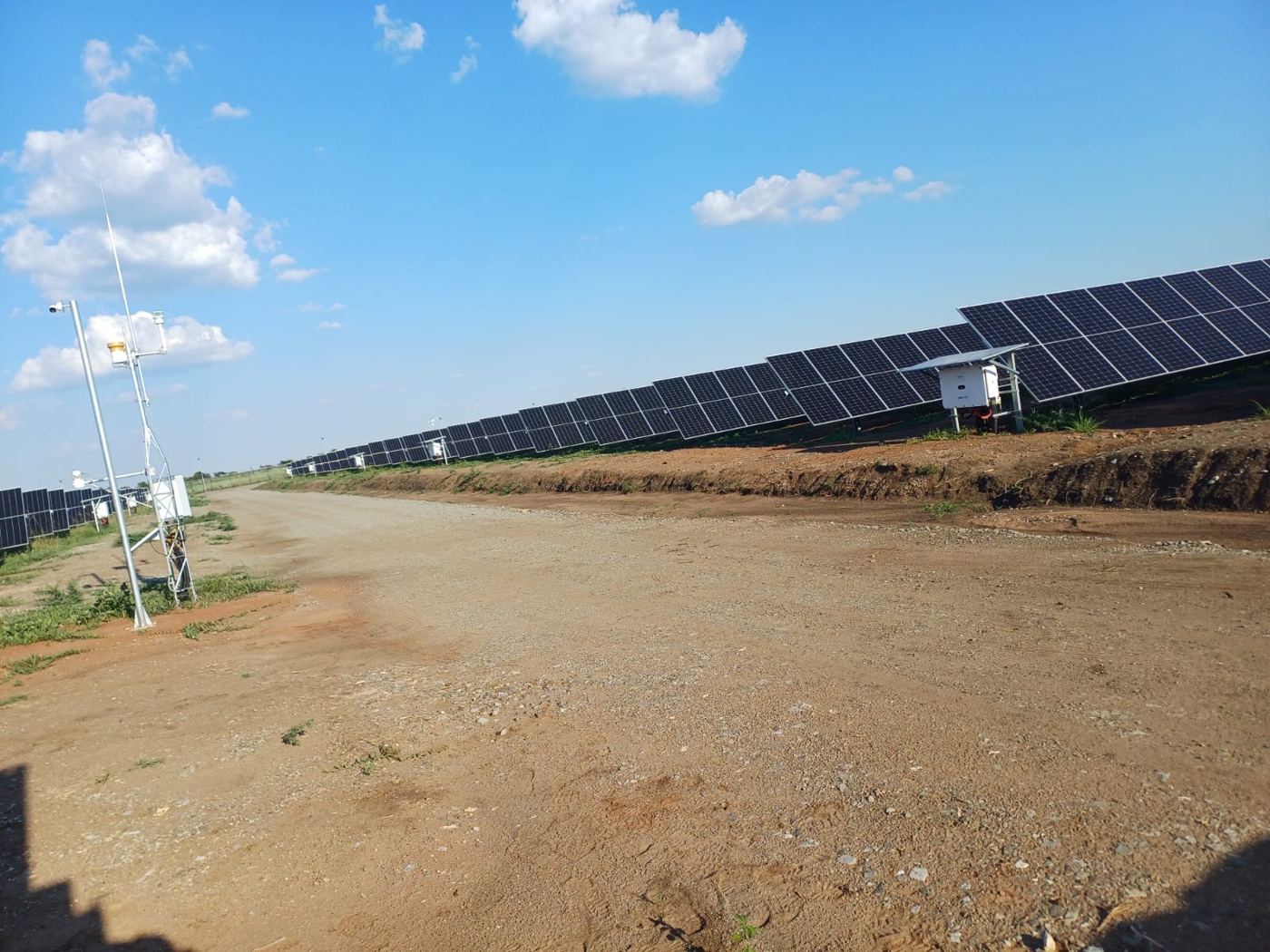 Meteorological station with camera and sensors beside rows of PV panels at a utility-scale solar plant